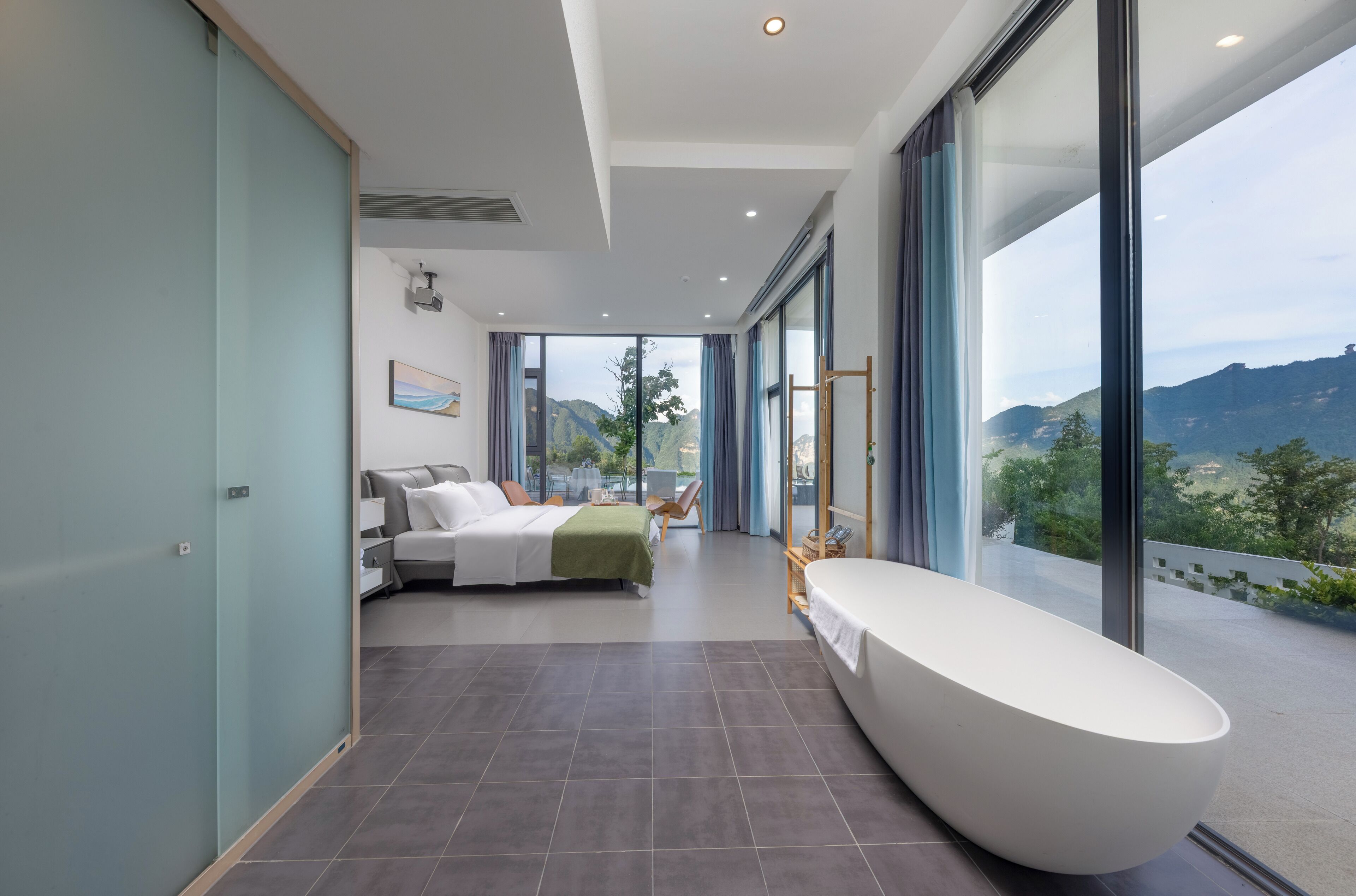 A modern bedroom with a large bed, a bathtub, and a view of a mountainous landscape.
