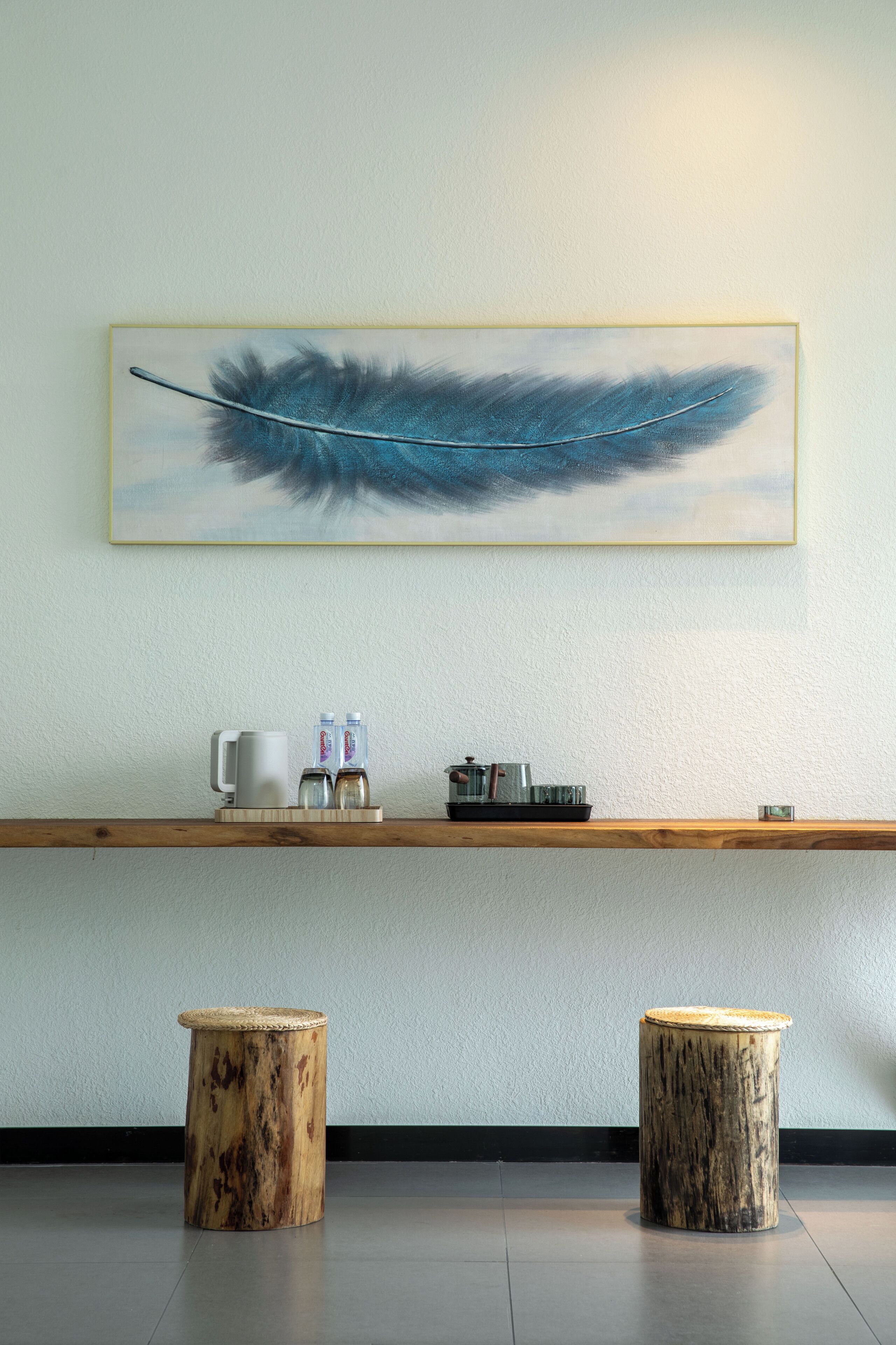 A modern interior with a wooden shelf displaying kitchenware, two wooden stools, and a feather artwork on the wall.