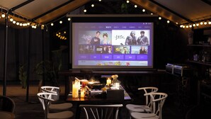 Un restaurante con una gran pantalla mostrando un menú, mesas con sillas e iluminación ambiental.