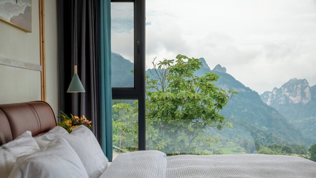 Un dormitorio con una cama grande, una ventana con vistas a las montañas y una lámpara colgante.