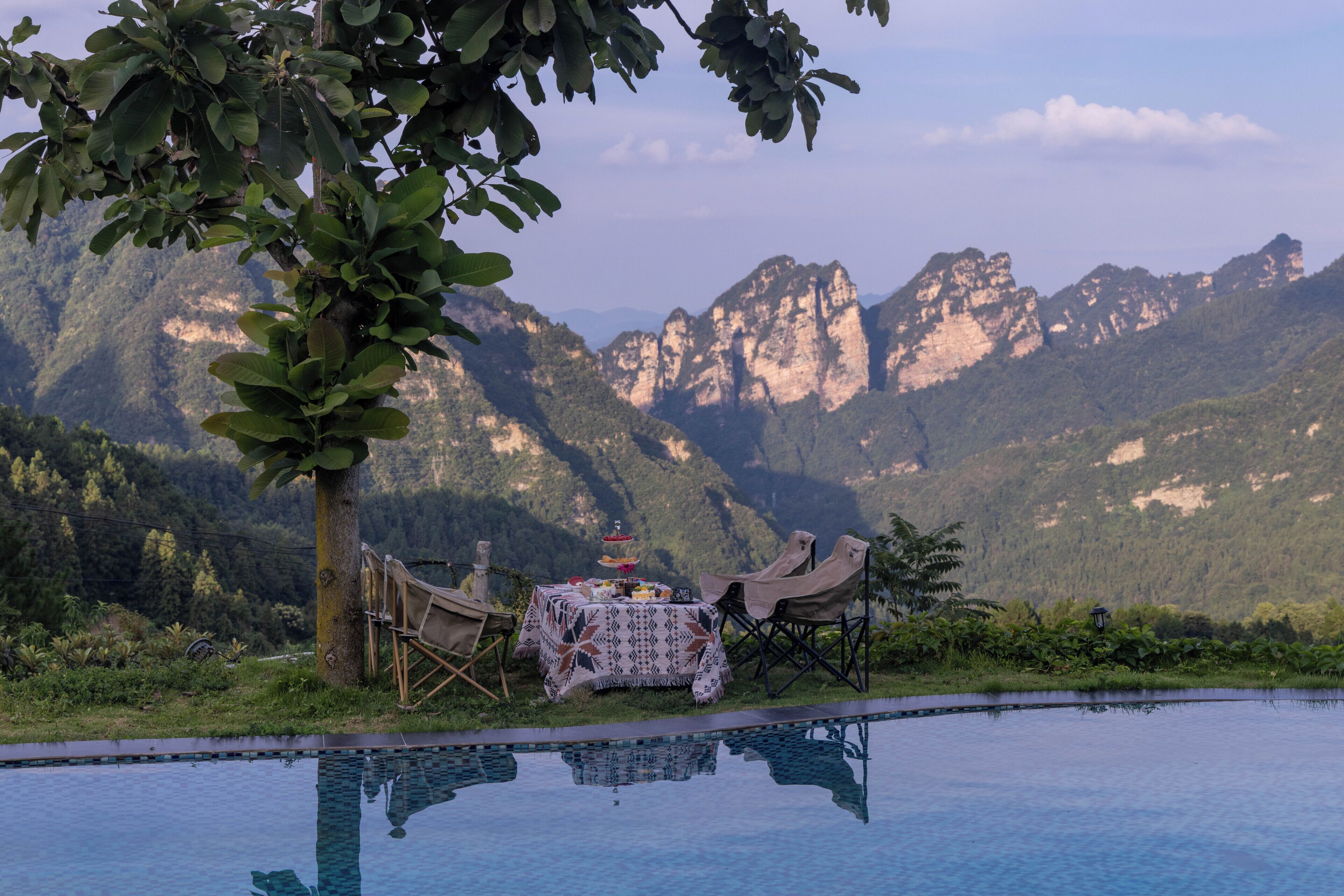 Un área de comedor al aire libre con mesa y sillas, piscina y un paisaje montañoso de fondo.