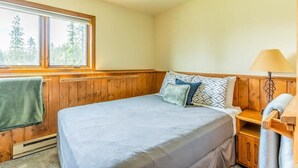 Un dormitorio con cama, ventana, lámpara y pared de madera.