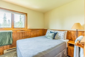 Ein Schlafzimmer mit einem Bett, einem Fenster, einer Lampe und einer Holzwand.