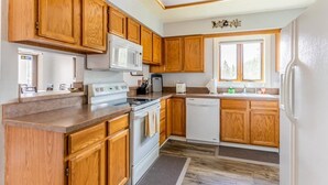 Cocina con armarios de madera, microondas, estufa, lavavajillas y ventana que proporciona luz natural.