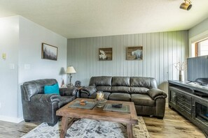 A living room with a brown leather sofa, a wooden coffee table, and a television on a cabinet. - Altitude Adjustment | Ski. Shred. Repeat. (Whitefish)
