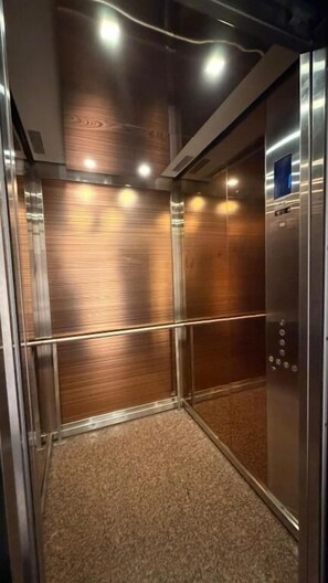 An elevator interior with metallic walls, a carpeted floor, and a control panel on the right. - Clowzer Al Rabea (Riyadh)