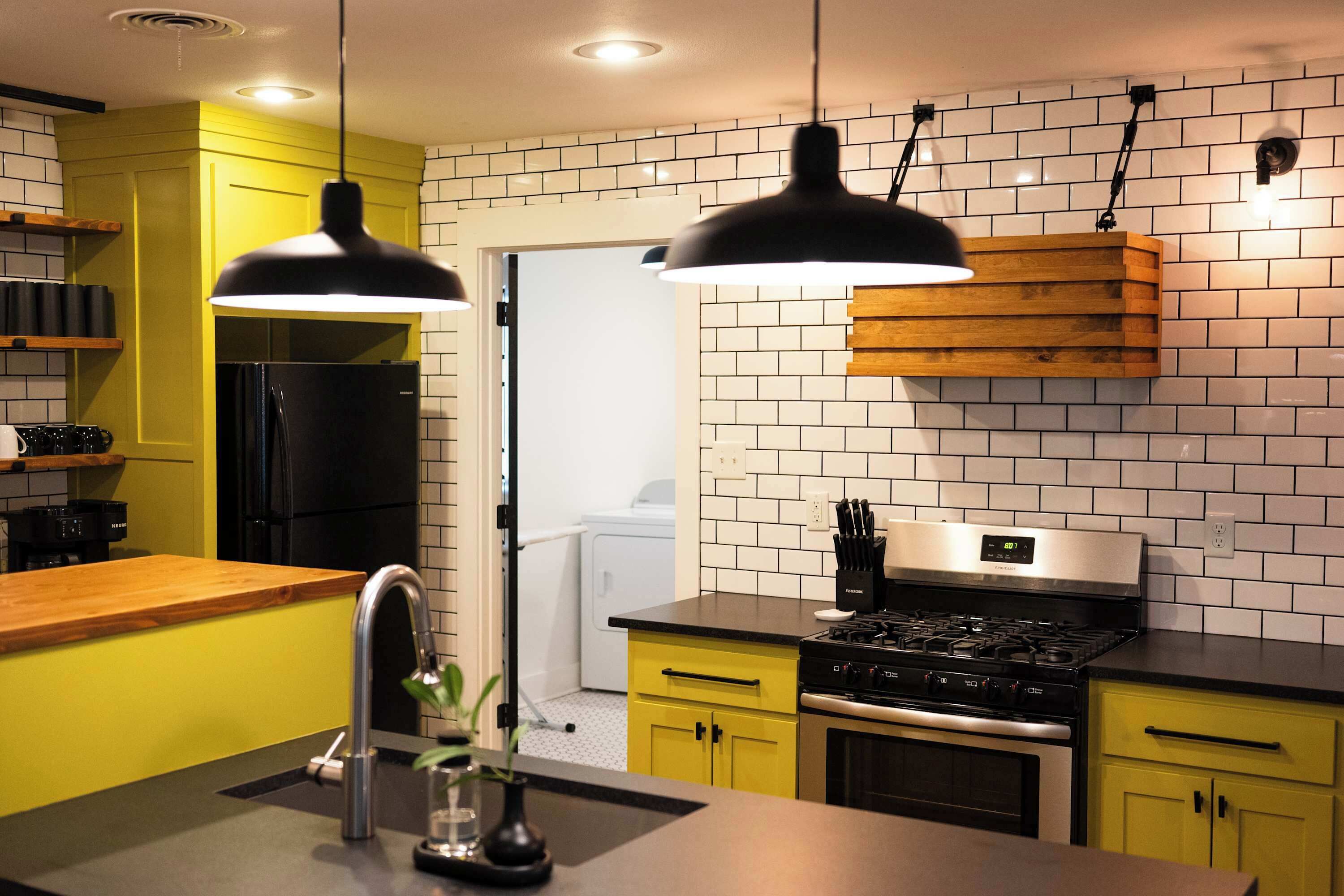 A modern kitchen with yellow cabinets, a black refrigerator, a stainless steel stove, and pendant lights.