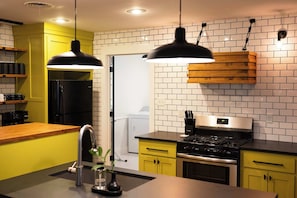 A modern kitchen with yellow cabinets, a black refrigerator, a stainless steel stove, and pendant lights. - Downtown Casa Verde - 0.5 mi UCA (Conway)