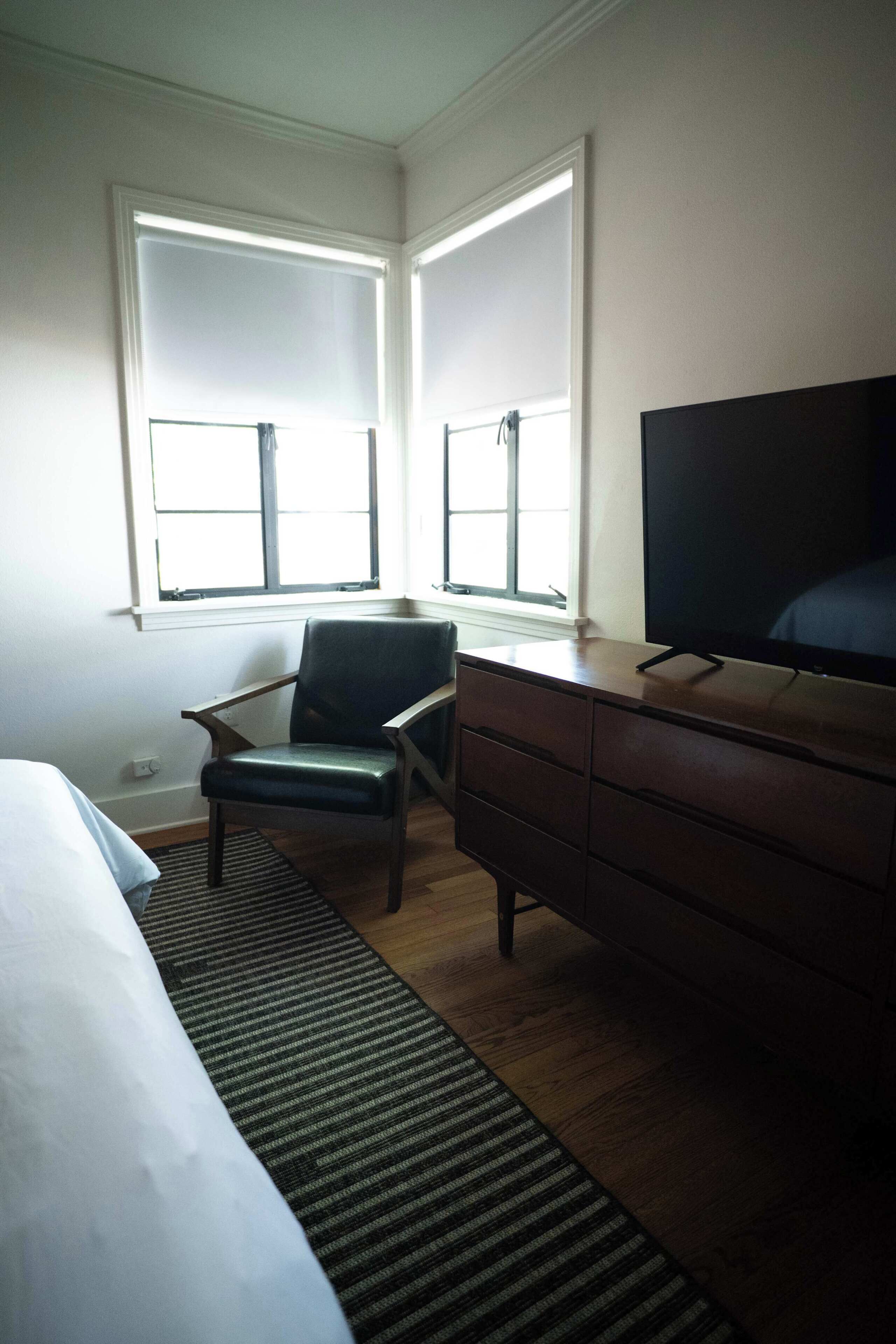 Une chambre d’hôtel équipée d’un lit, d’un bureau, d’une chaise, d’une télévision et de deux fenêtres.