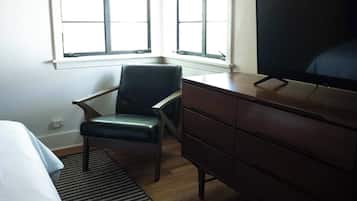 A hotel room with a bed, a desk, a chair, a television, and two windows.