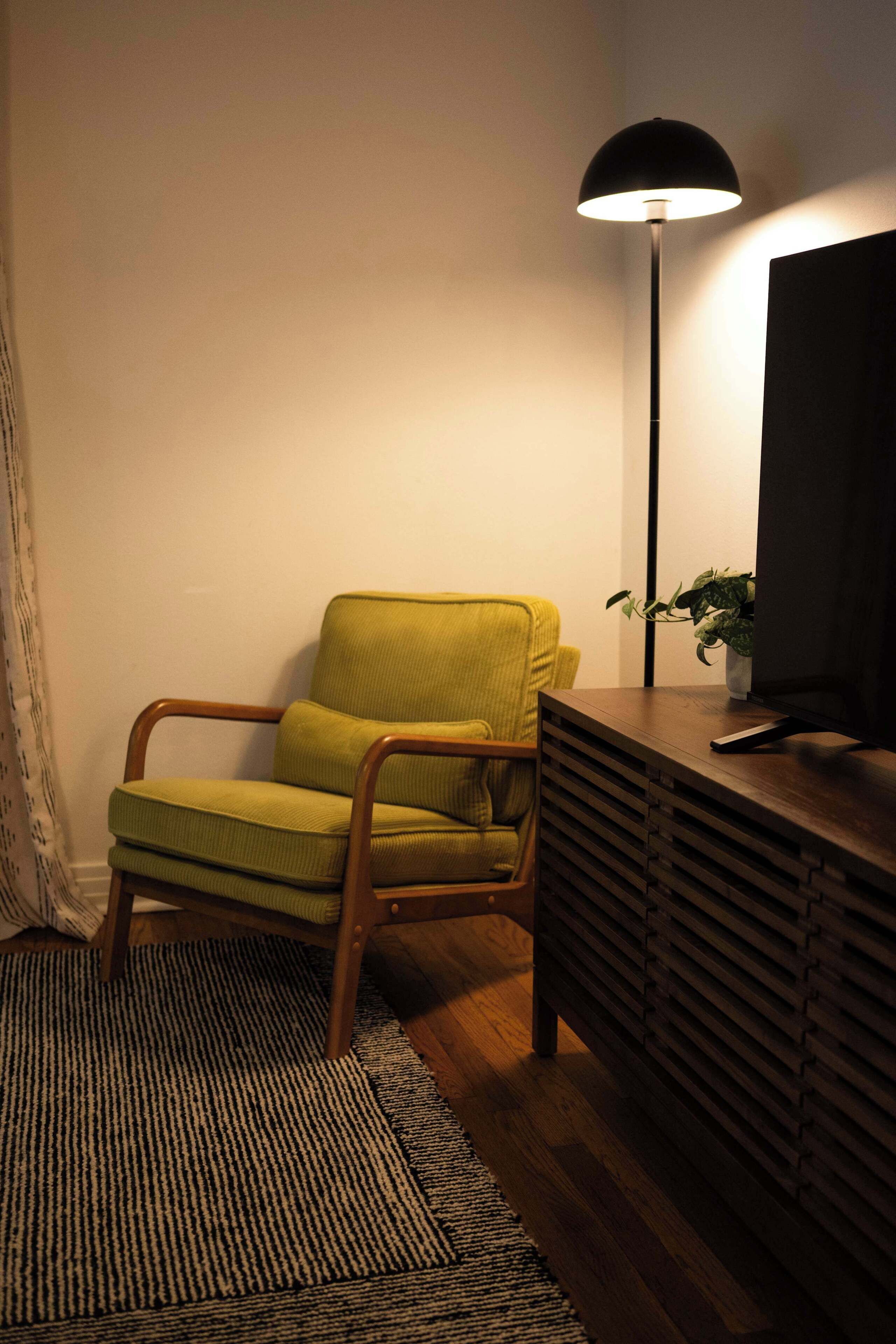 A room with a green armchair, a black floor lamp, a wooden side table, and a television.