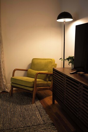 A room with a green armchair, a black floor lamp, a wooden side table, and a television.