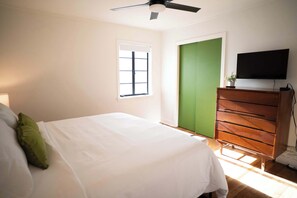 A bedroom with a bed, a dresser, a television, a window, and a door.