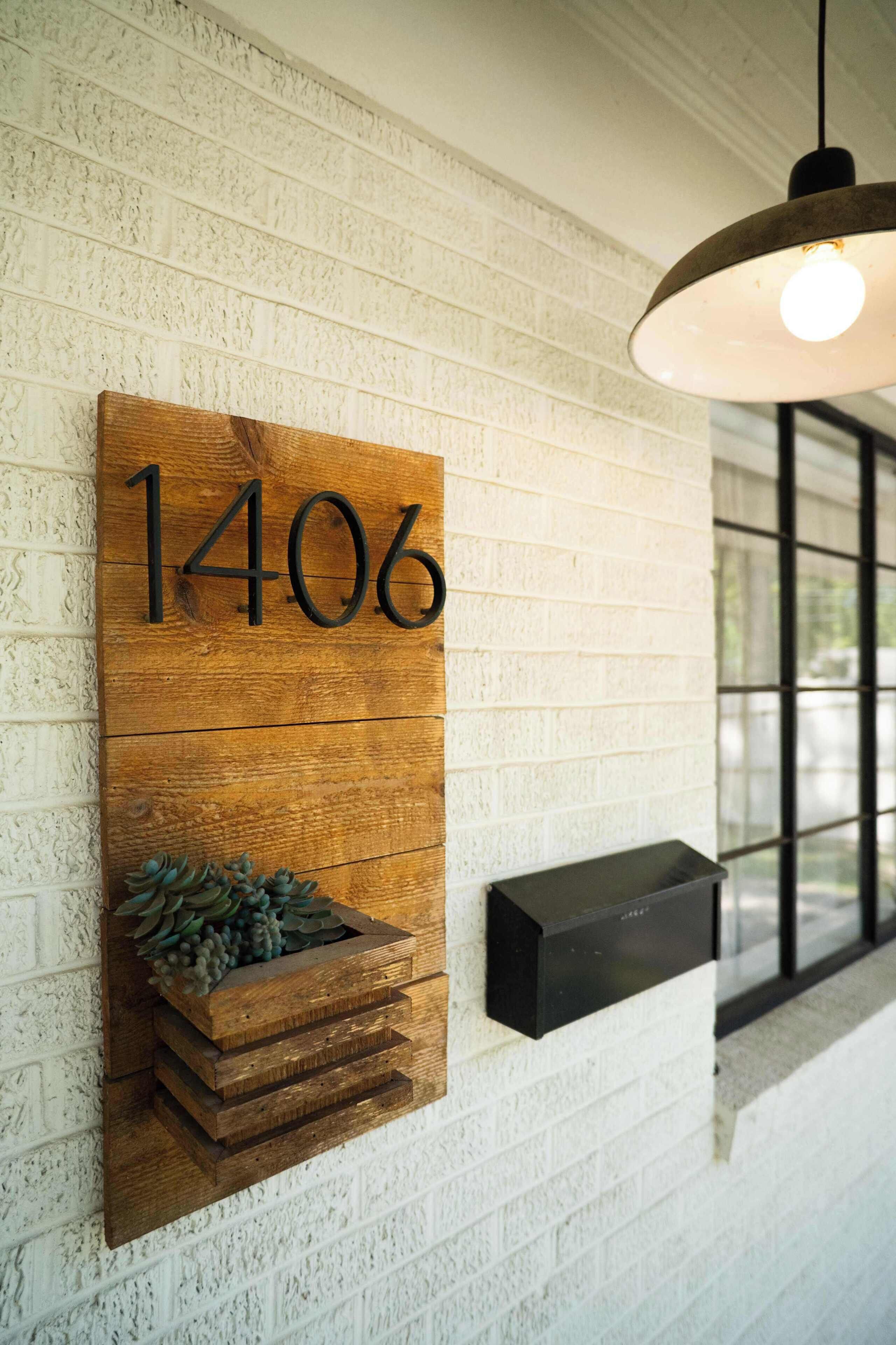 A wooden number sign with the number 1406 on a textured wall, a hanging light fixture, and a black rectangular object on the wall.