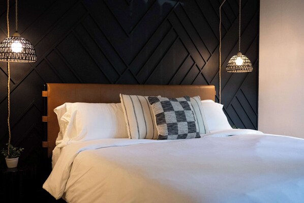 A bed with white bedding, a wooden headboard, and two hanging light fixtures.