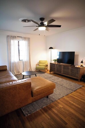 A living room with a sofa, a small table, a TV, and a ceiling fan. - Downtown Casa Verde - 0.5 mi UCA (Conway)