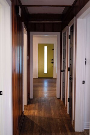 A hallway with wooden floors and white doors, leading to a room with a green door.