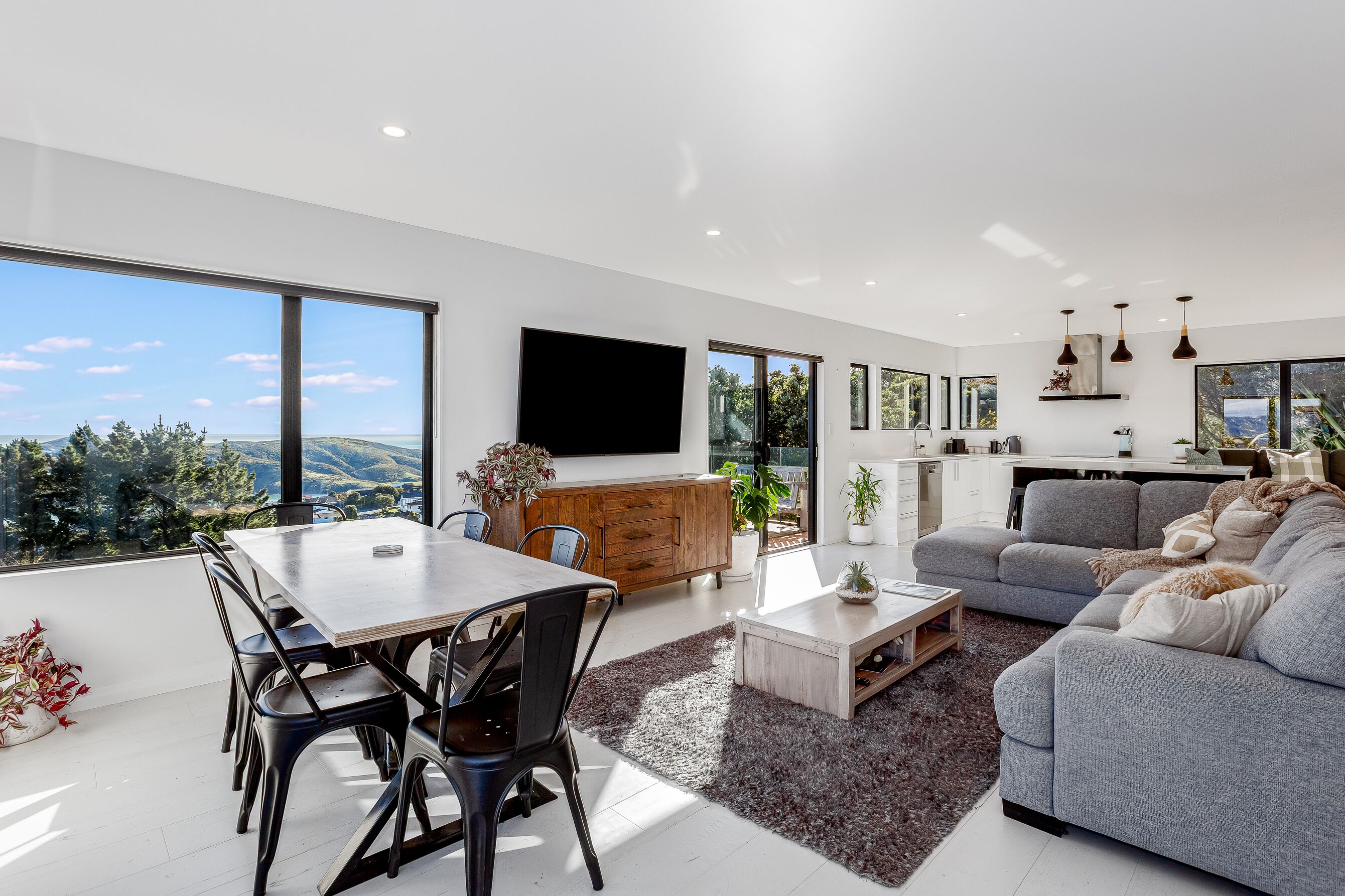 A modern living space with a dining area, a sofa, and a kitchen.