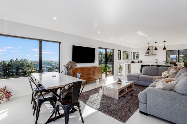 A modern living space with a dining area, a sofa, and a kitchen.