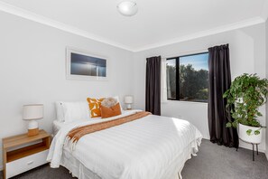 A hotel room with a bed, bedside tables, a window with curtains, a plant, and a wall-mounted picture.
