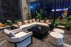 Un área de descanso moderna con un sofá modular, un taburete redondo y una mesa de centro de vidrio.