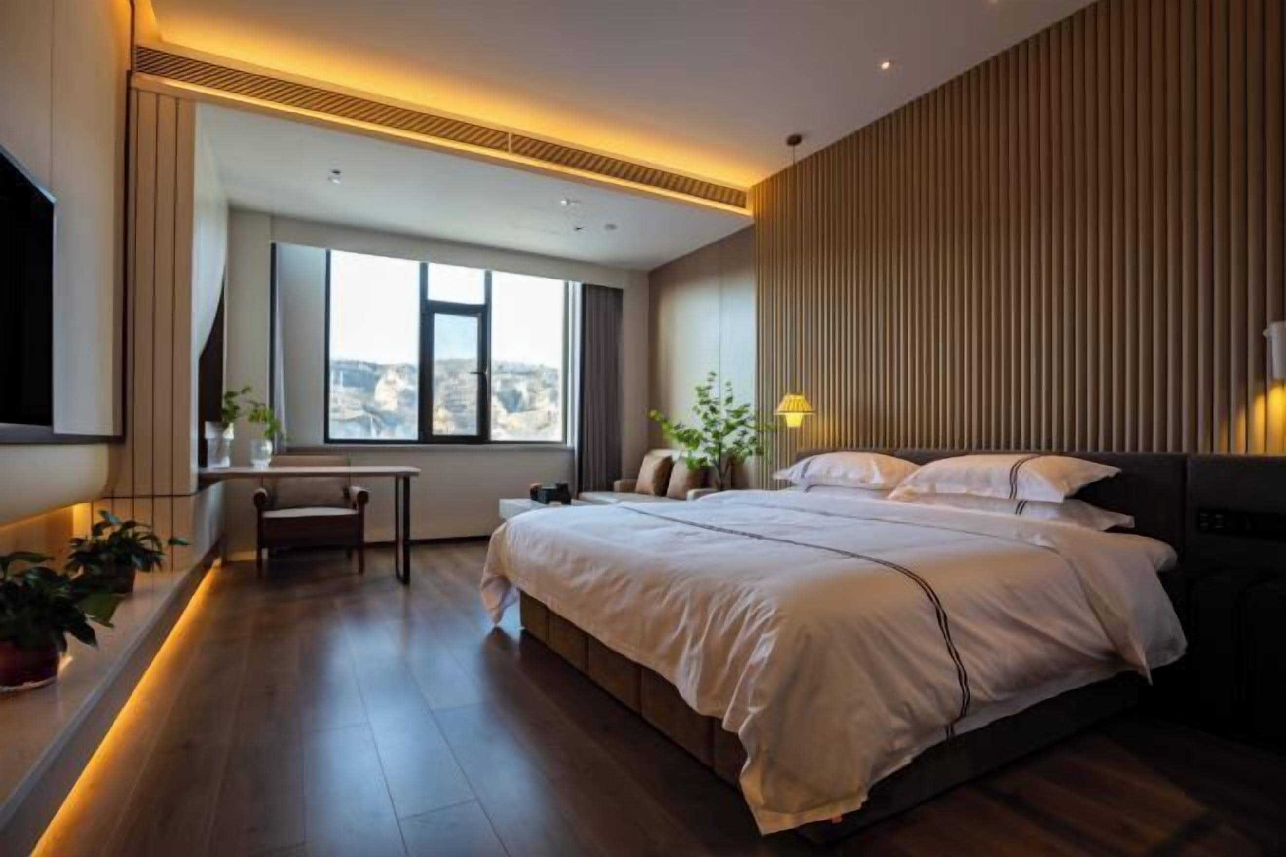 A modern hotel room with a large bed, a desk, and a view of the city.