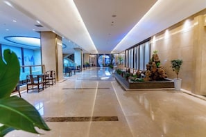 Un amplio vestíbulo de hotel con una zona de estar central, una recepción y una decoración vegetal.