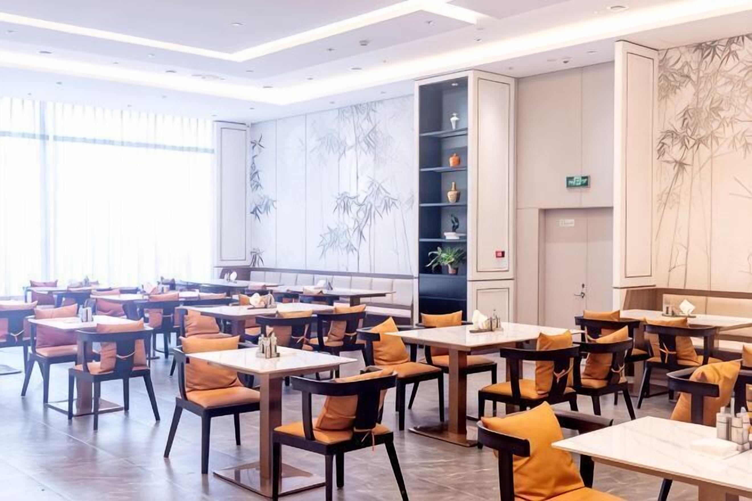 Un restaurante con varias mesas y sillas, una pared decorada con motivos de bambú y un estante con objetos decorativos.