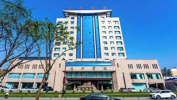 A multi-story hotel with a prominent blue and beige facade, a large entrance, and a parking area with cars.