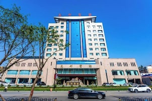 Un hotel de varios pisos con una fachada llamativa en azul y beige, una entrada espaciosa y un estacionamiento con automóviles.