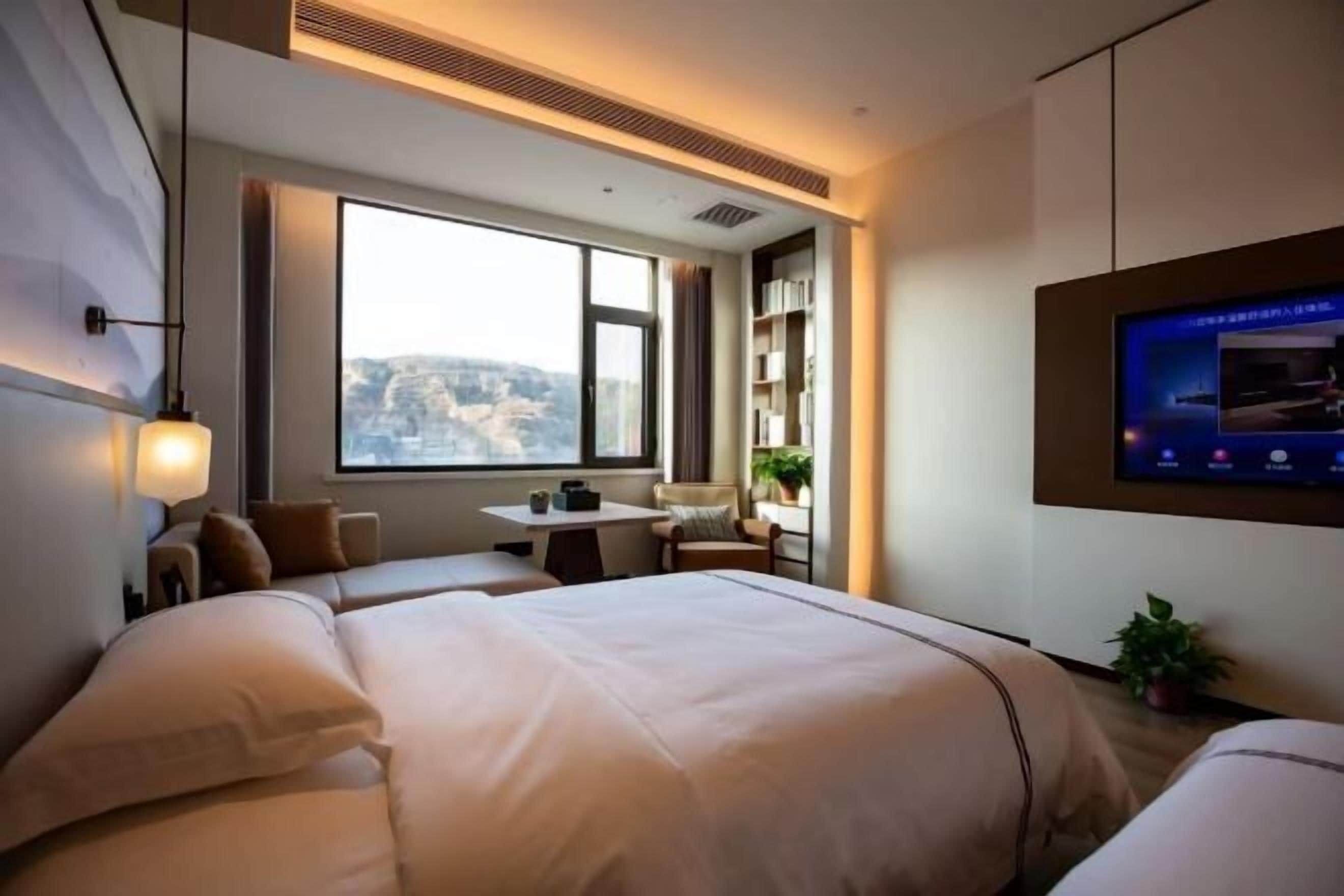 Quarto de hotel com uma cama grande, uma escrivaninha e uma televisão na parede.