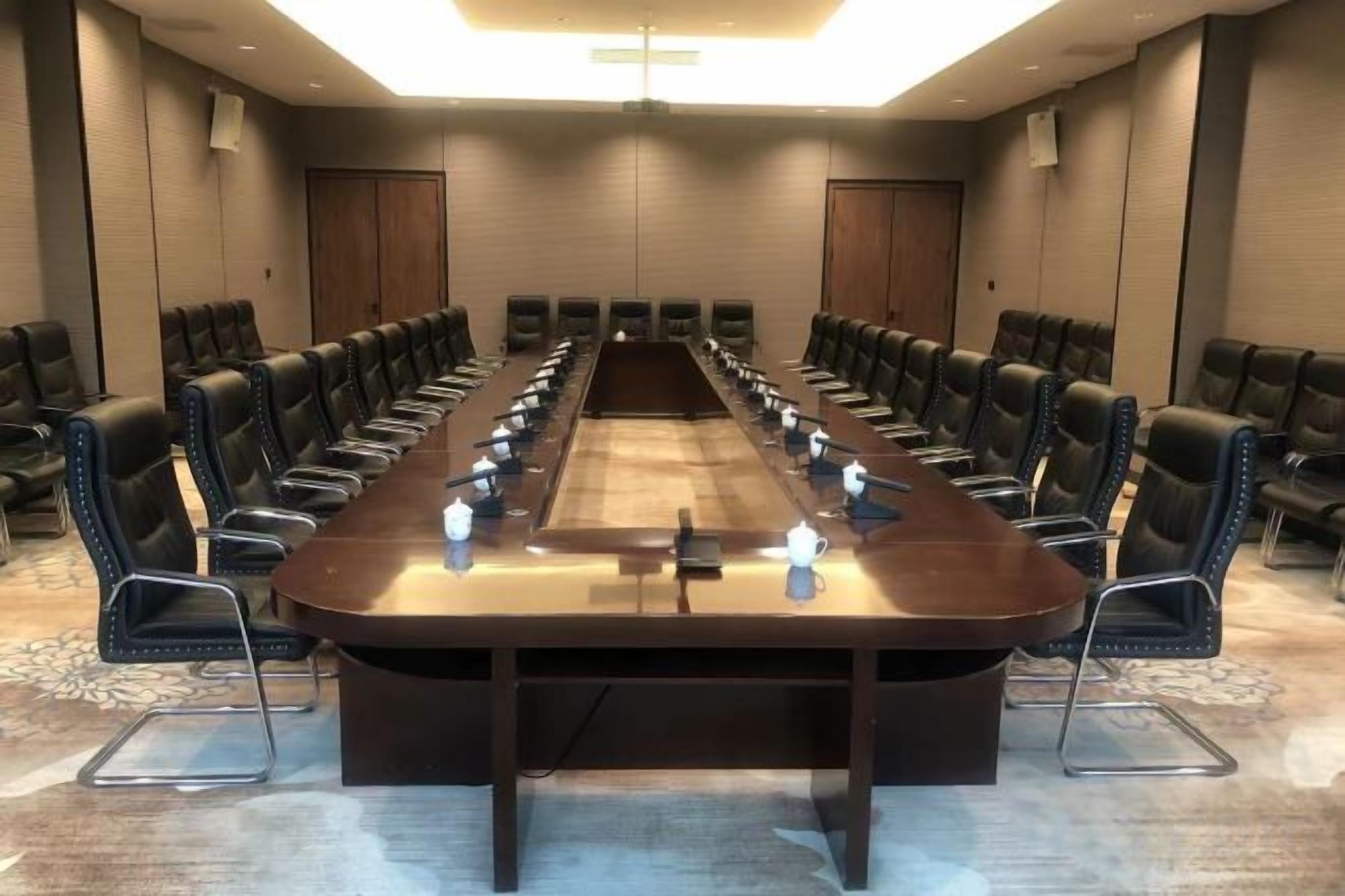 Un salón de conferencias con una larga mesa, varias sillas y micrófonos.