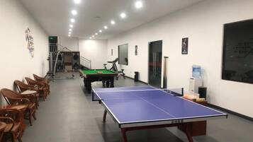 Una habitación con mesa de ping pong, sillas, mesa de billar y dispensador de agua.