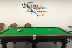 A pool table with a cue ball and a red and white striped ball, surrounded by four chairs.