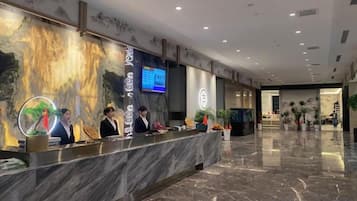 Et hotellets reception med en marmor disk, personale, en digital skærm og et stort vægmaleri.