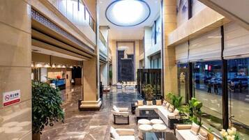 A hotel lobby with a central seating area, a reception desk, and a view of the street through large windows.