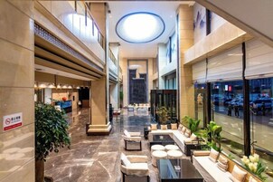 A hotel lobby with a central seating area, a reception desk, and a view of the street through large windows.