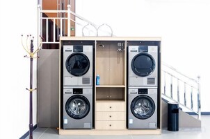 A laundry facility with two washing machines and a dryer, a staircase, and a railing.