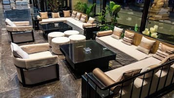 Un área de estar moderna con sofás, otomanas y una mesa de centro, dispuesta alrededor de un separador de vidrio.