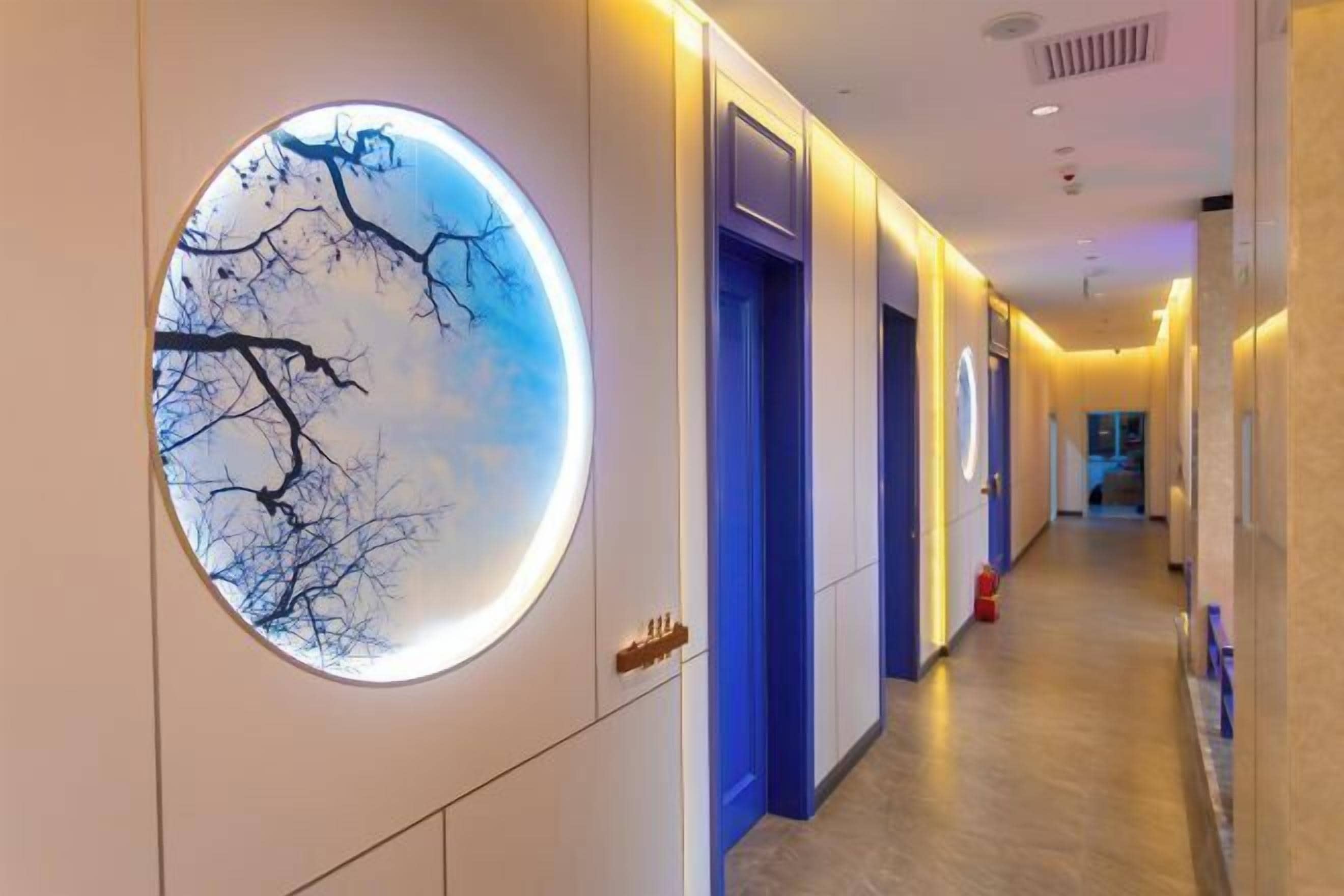 A hotel corridor with a circular wall art, blue doors, and a fire extinguisher.