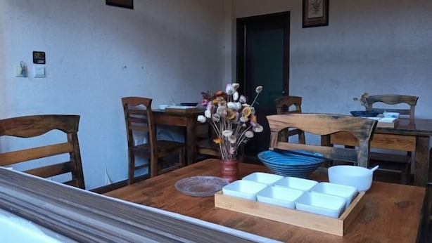 A dining area with a wooden table, chairs, a vase with flowers, and a tray of white bowls. - Tengchong Yinghe sightseeing Inn (Tengchong)