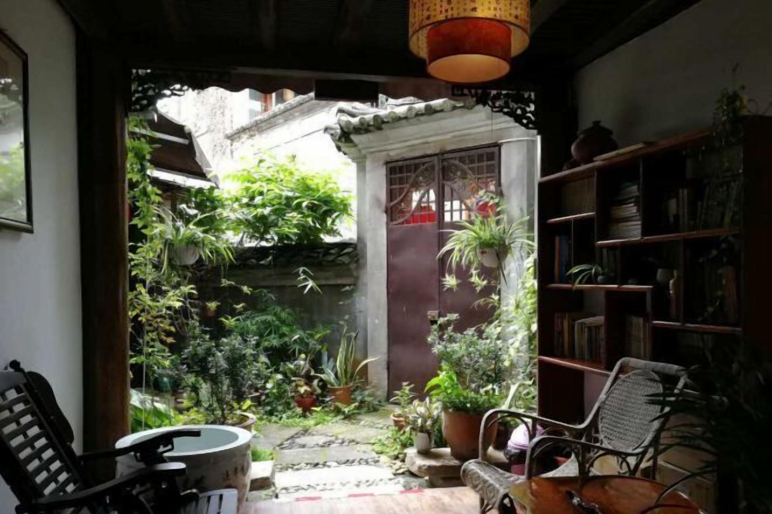 Una habitación con vistas a un jardín, una estantería y un sillón.