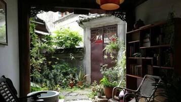 Una habitación con vistas a un jardín, una estantería y un sillón.