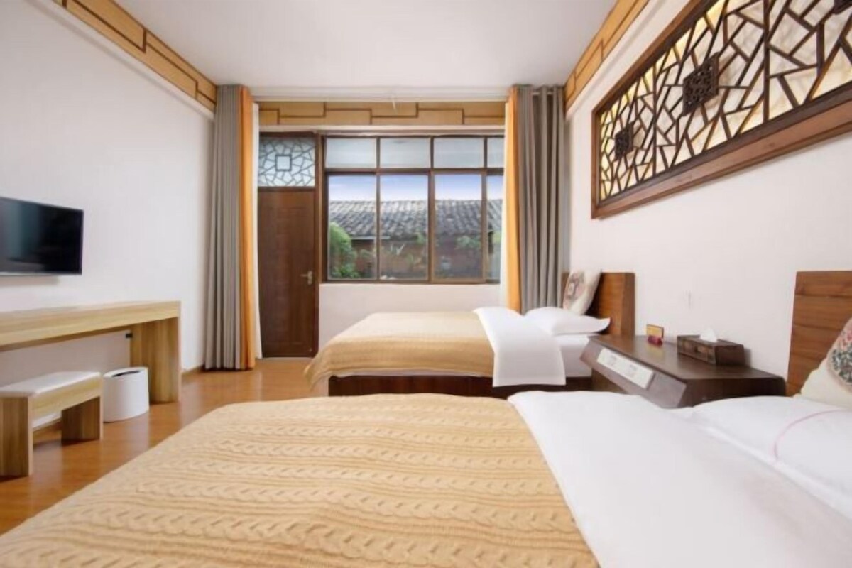 A hotel room with two beds, a desk, a TV, and a view of the outdoors.