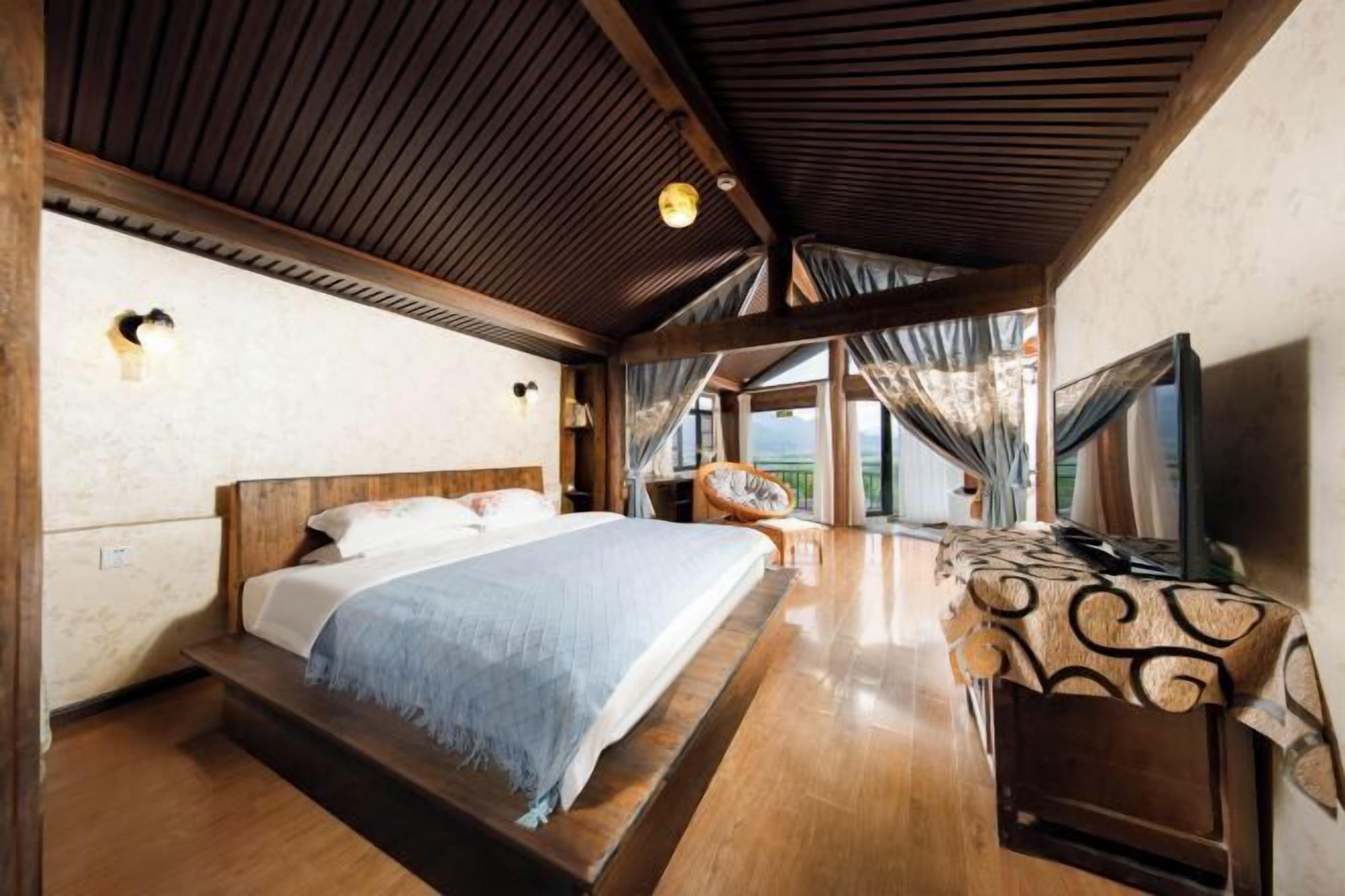 A bedroom with a large bed, a desk, and a view of the outdoors.