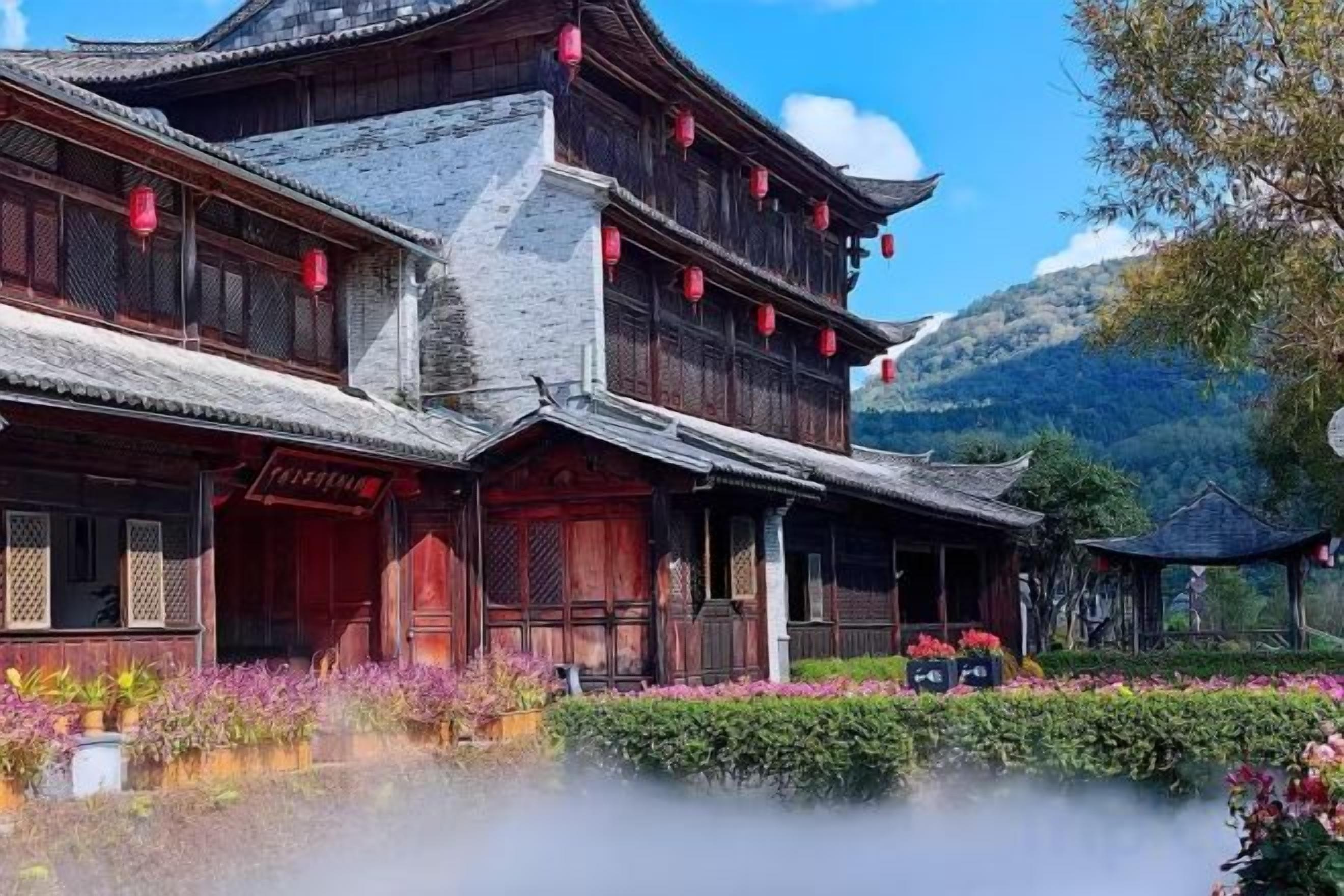 A traditional wooden building with multiple levels, a tiled roof, and a garden with flowers and a pond.