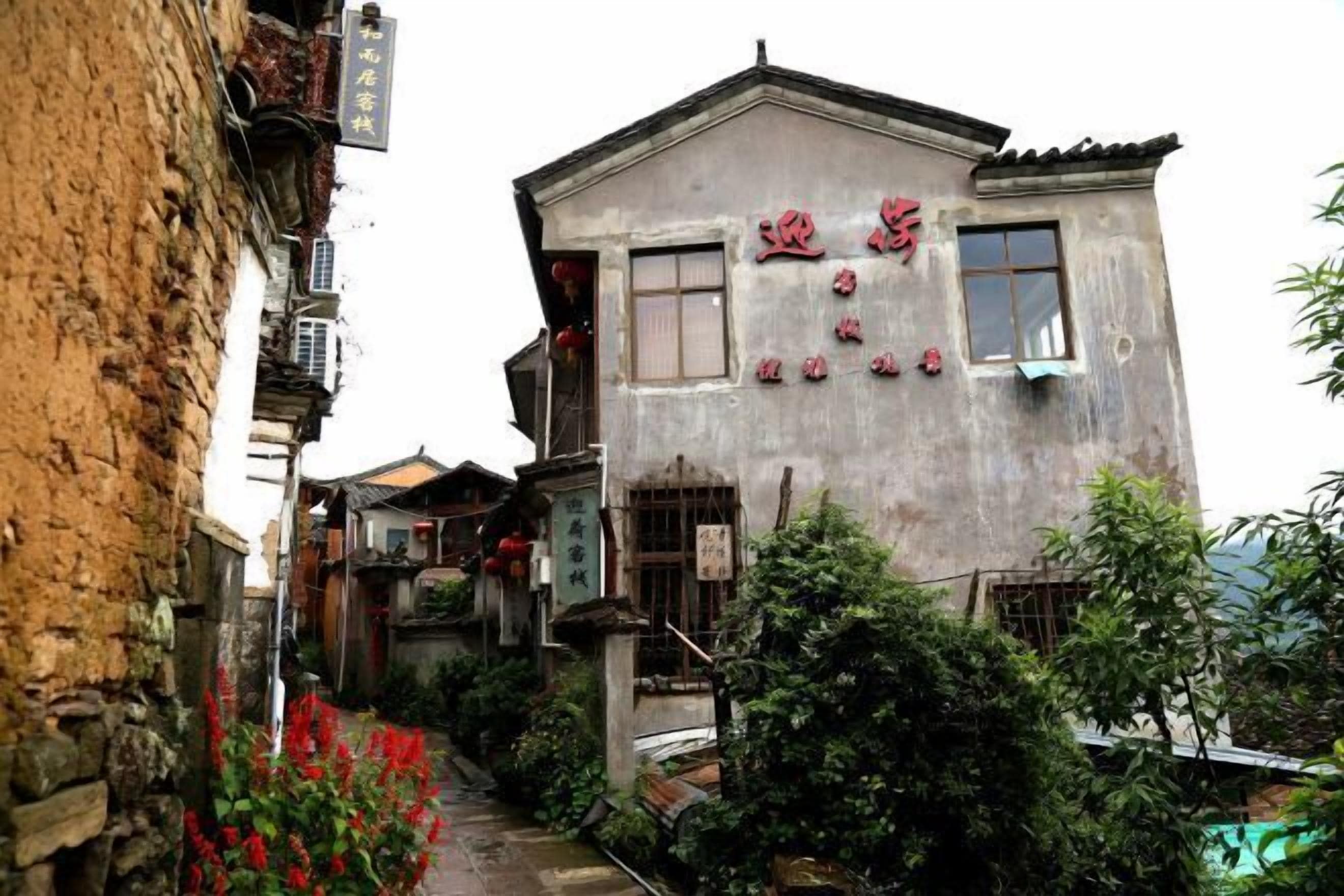 A traditional building with a signboard, a narrow alleyway, and some greenery.