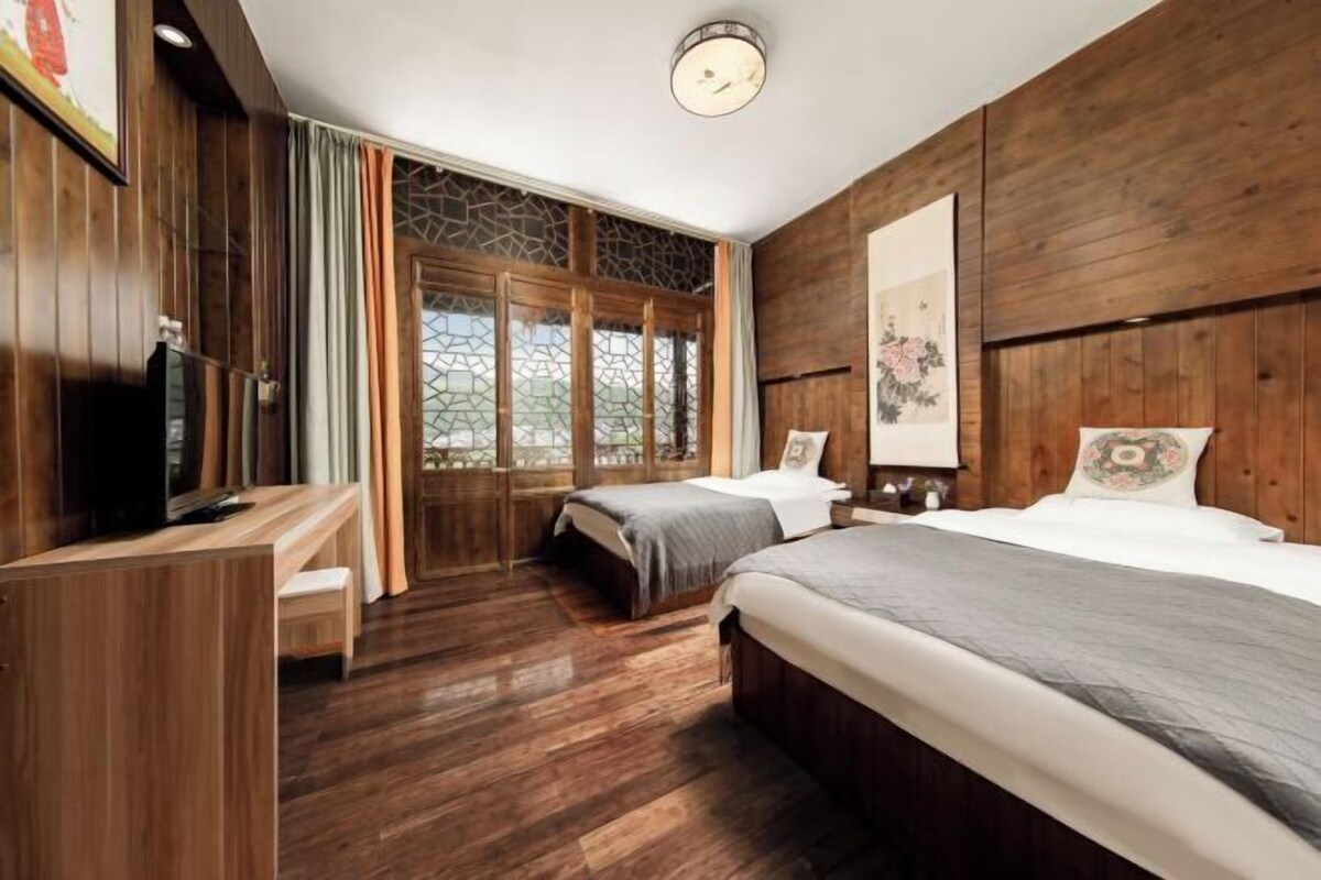 A room with two beds, a desk, and a large window with curtains.