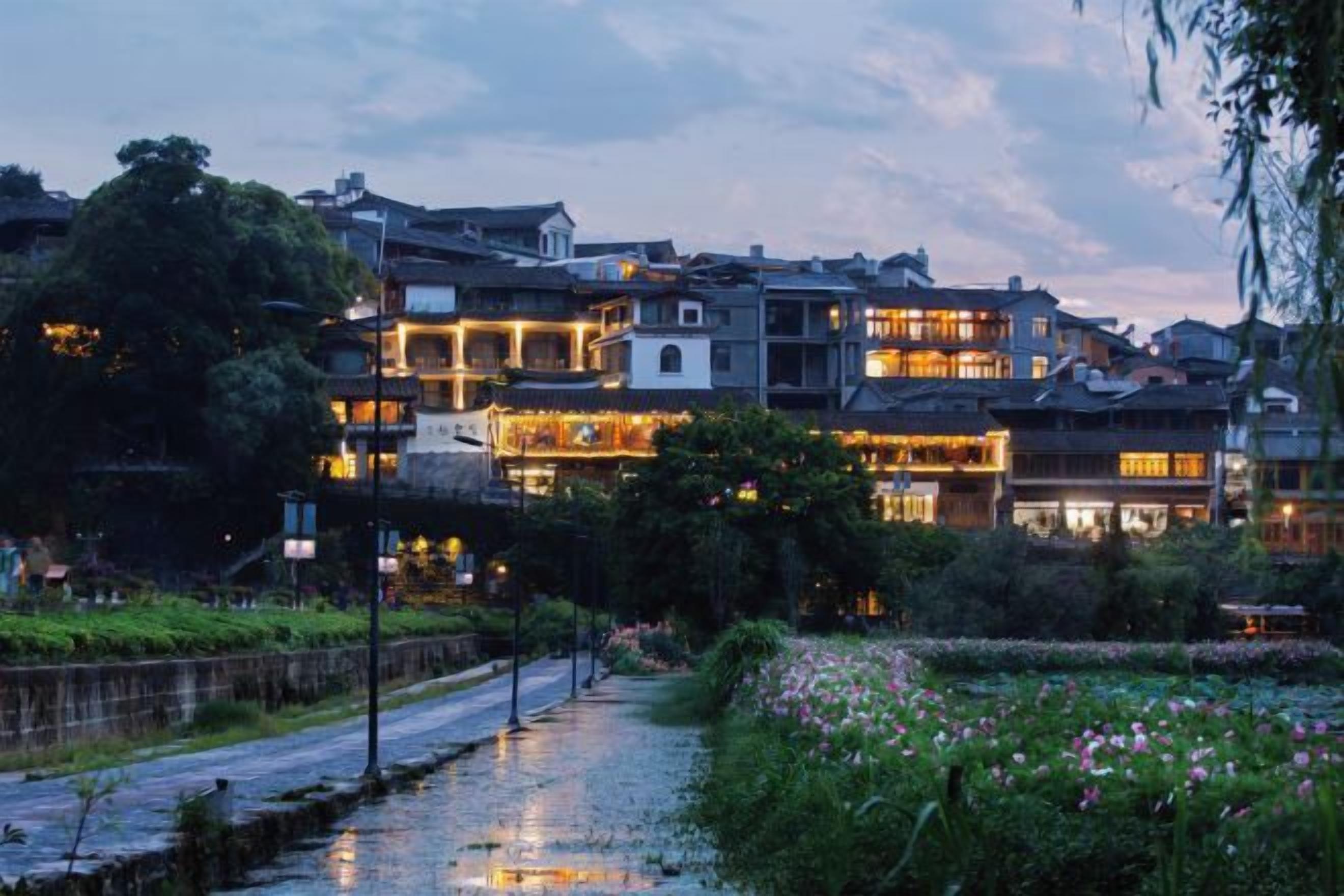 A traditional building with multiple stories, a paved pathway, and a garden with pink flowers.