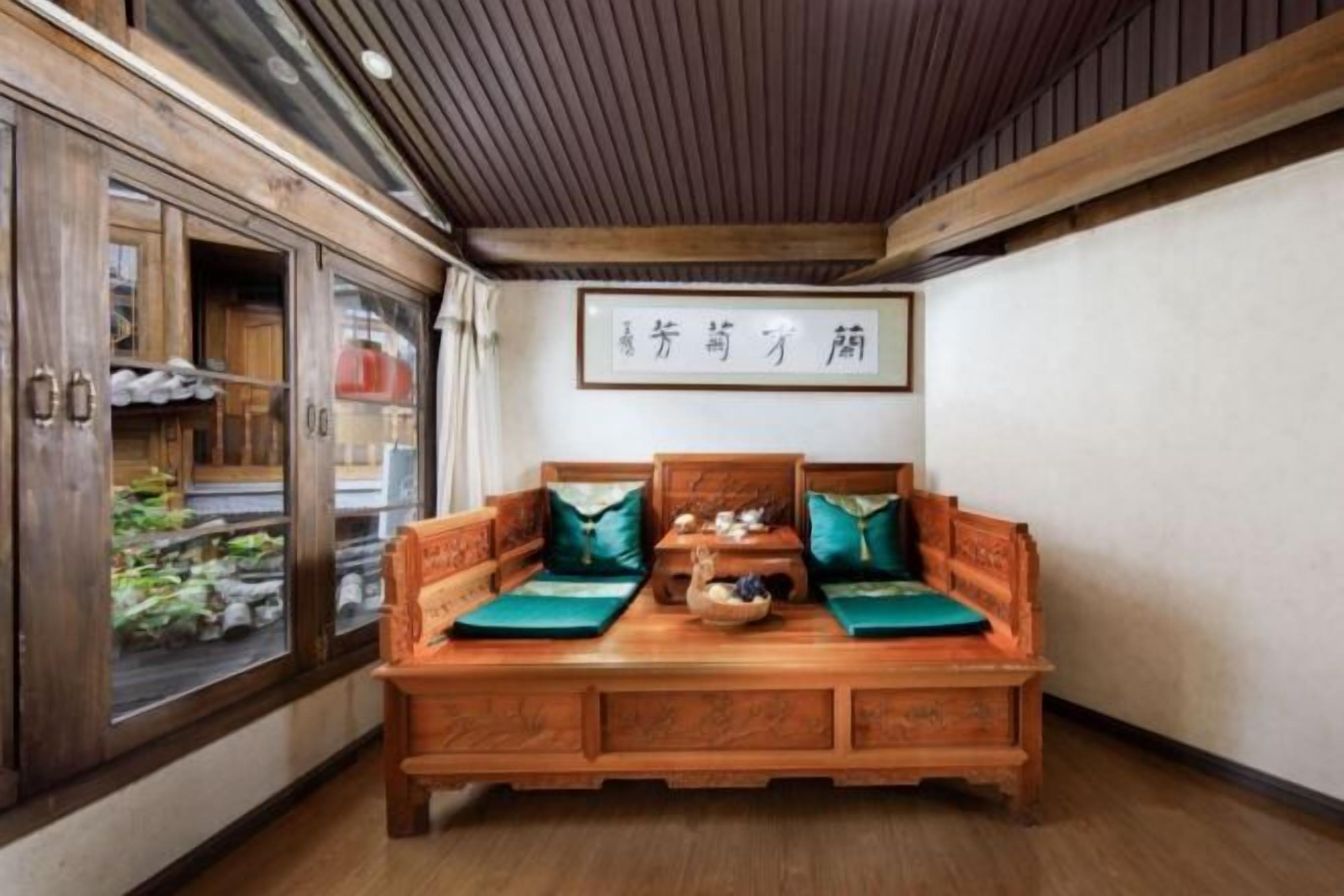 A traditional wooden sofa with cushions, a wooden cabinet with glass doors, and a wall-mounted sign.